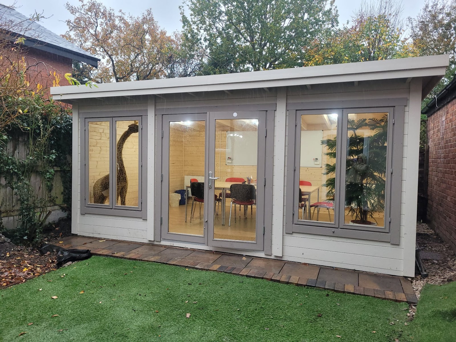A timber garden studio repainted in a warm dove grey, framing a tidy home-office space within.