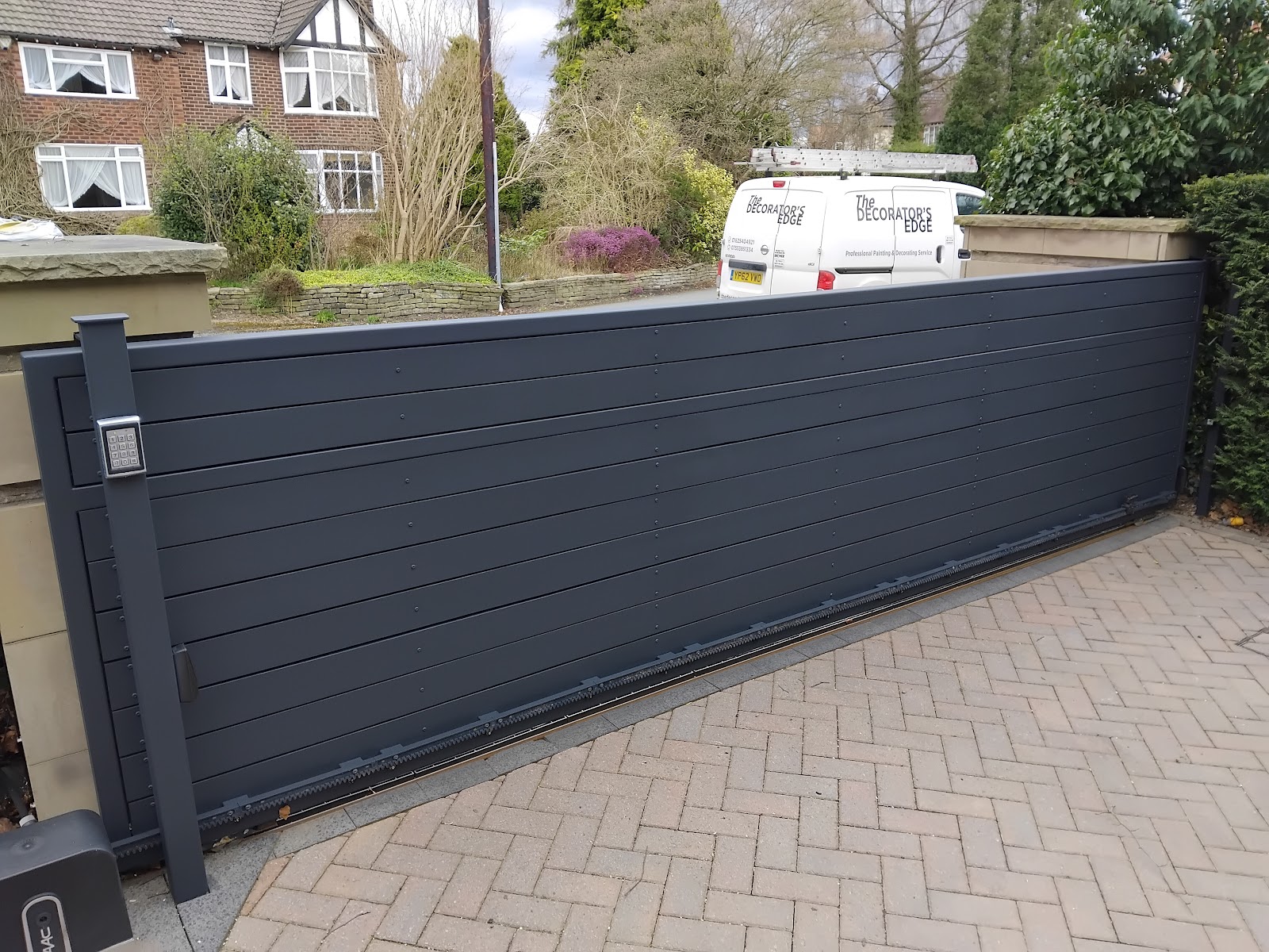 A long sliding driveway gate and fence finished in anthracite grey — the branded van on site throughout the job.
